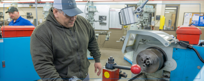 Student operating a metal lathe machine in a technical training lab