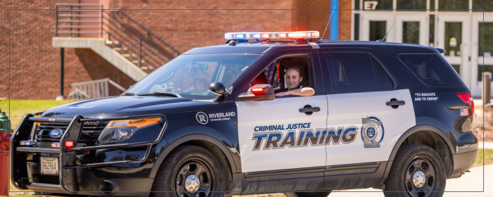 Riverland Criminal Justice training vehicle with student inside and emergency lights activated